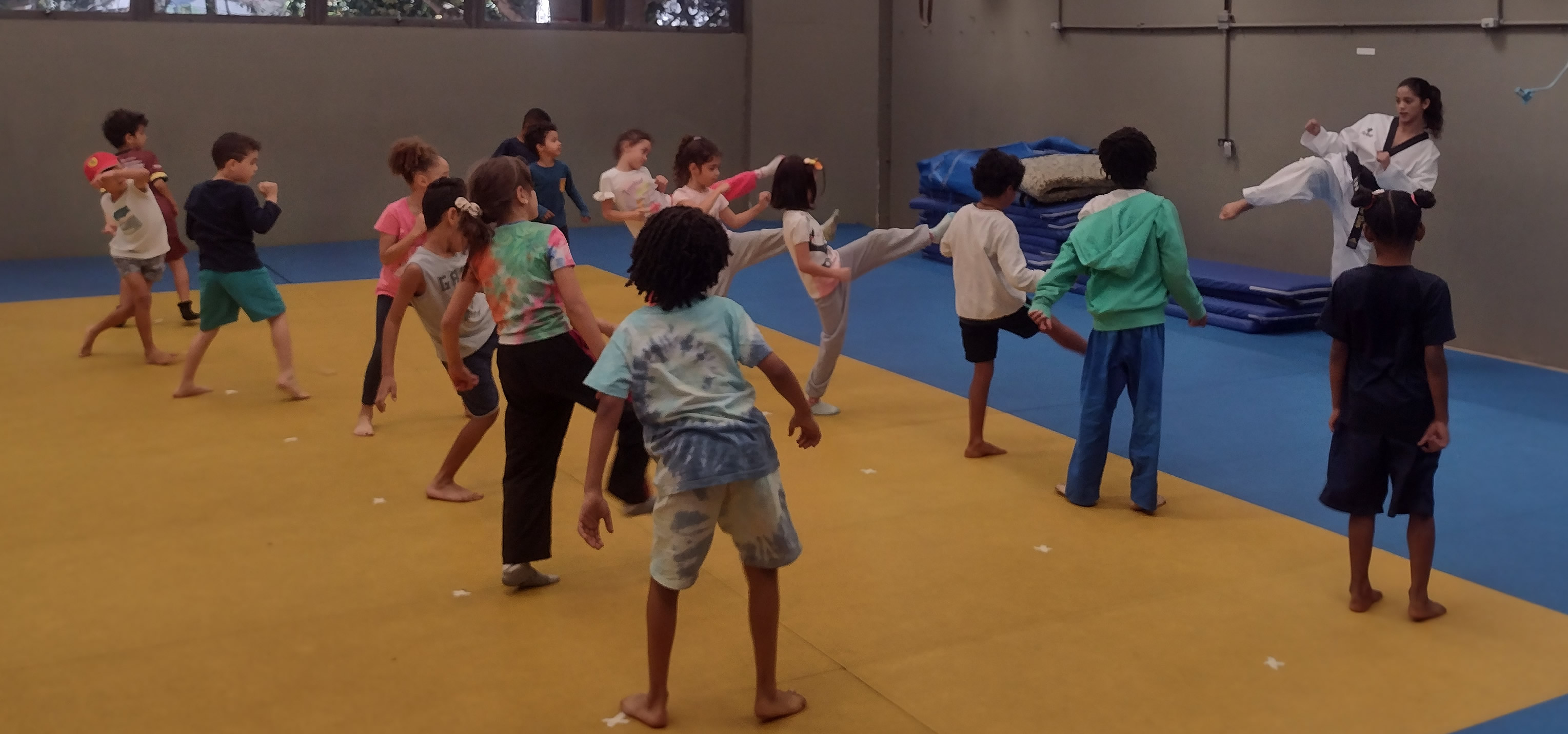 Aula de iniciação de Taekwondo com crianças no tatame do CTE/UFMG, sob a orientação de instrutora faixa preta.